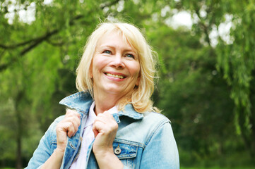 Beautiful blonde woman in a denim jacket in a spring park. Elderly happy lady pensioner. Close up.