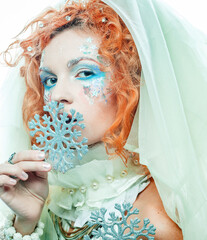 woman with a bright creative make-up in a New Year's style holds a silver snowflake near her face.