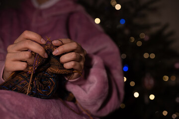 a woman knitting needles by the Christmas tree. A cozy winter evening at home. A gift made with his own hands.