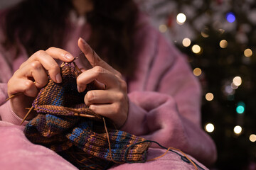 a woman knitting needles by the Christmas tree. A cozy winter evening at home. A gift made with his own hands.