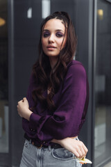 Young woman in purple blouse poses confidently against urban backdrop