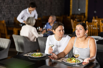 Young woman and adult woman have dinner and drink wine together in restaurant