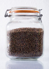 Glass bottle of dry lentils on white background