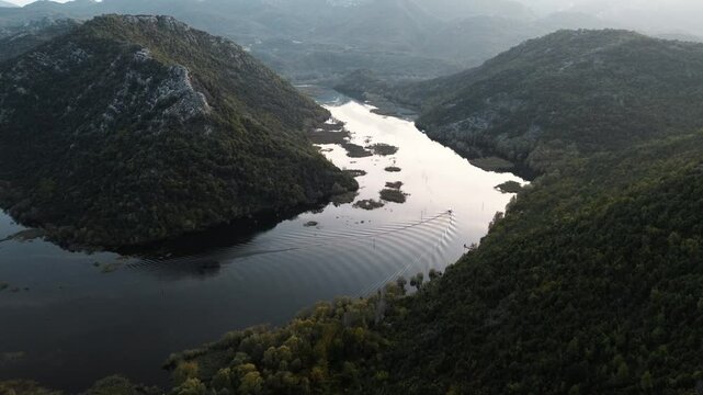 Rijeka Crnojevica near Skadar lake in Montenegro at sunset. A winding river among the rocky mountains. Breathtaking landscape aerial view. A tourist boat is sailing fast along the river.