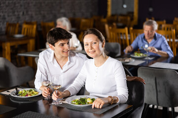 Smiling guy and girl talking and joking merrily during dinner at restaurant. Young male and female colleagues have fun chatting spend time in restaurant after working day