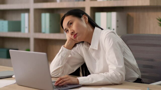 Bored tired exhausted Asian Korean business woman female worker entrepreneur Japanese Chinese businesswoman girl typing laptop working computer boring work unmotivated job task thinking indoor office