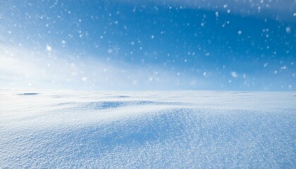 Clear snow-covered wavy field with snowflakes flowing through blue sunny sky giving winter holiday atmosphere. Background with copy space for text.