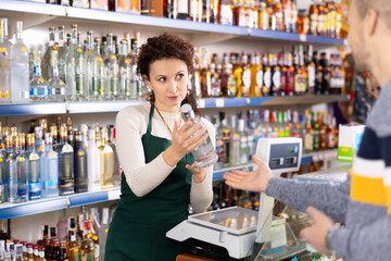 Woman seller near a cash register offers to buy a bottle of vodka to a man
