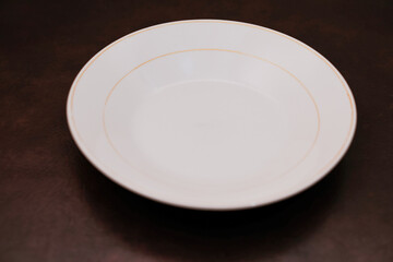 Empty white ceramic plate with orange circle isolated on brown background, eating place setting.