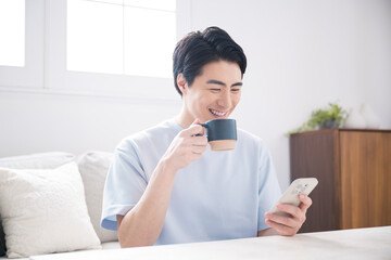 明るい部屋でスマホをタップし検索や操作するハンサムな笑顔の男性