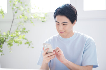 明るい部屋でスマホをタップし検索や操作するハンサムな男性