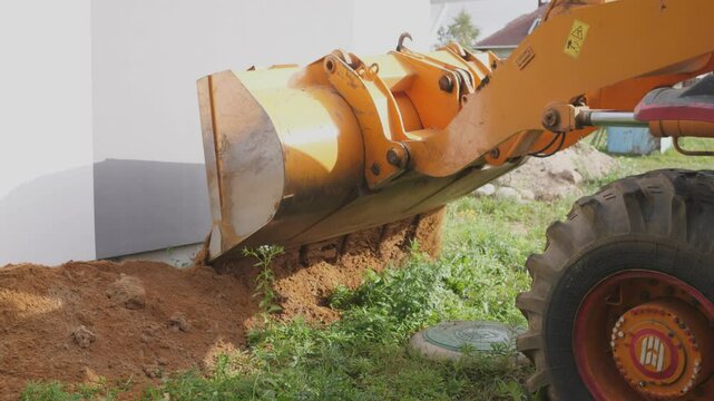 Excavation work is being carried out by a backhoe loader in close proximity to a foundation wall segment