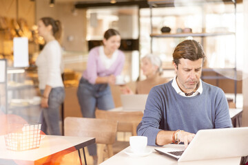 Focused man drinking coffee while working on laptop in cozy cafe