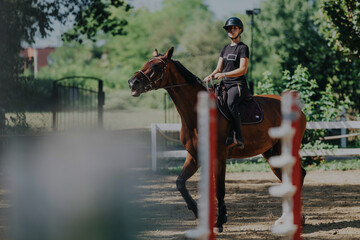 A confident equestrian rides a brown horse in a sandy training arena surrounded by lush greenery....