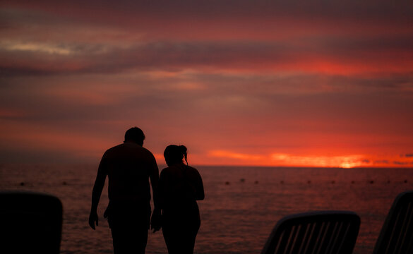 pareja caminando en la playa al atardecer con cielo rojizo 