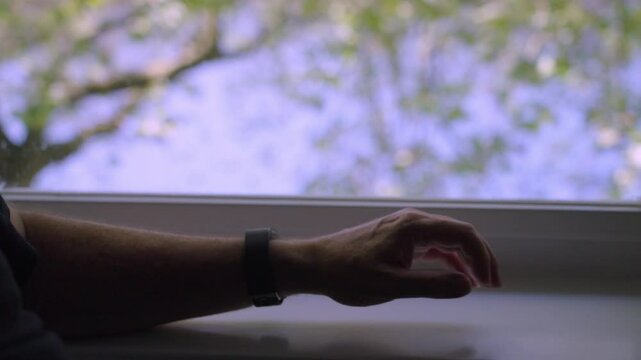 Man checking watch while resting arm on bright window sill during daytime