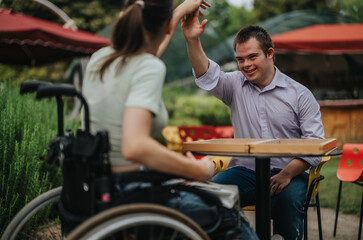 A boy with Down syndrome high-fives a girl in a wheelchair while playing backgammon at an outdoor...