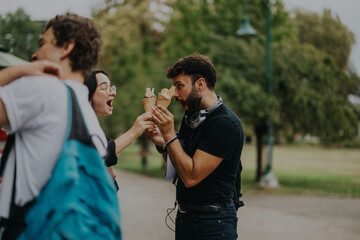 Obraz premium Group of diverse students having fun with ice cream in a park during a study break. The image captures a joyful moment of friendship and relaxation outdoors.