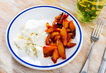 On white plate, portion of grainy cottage cheese with sour cream and peach slices in sugar syrup. Dish is complemented with mint tea