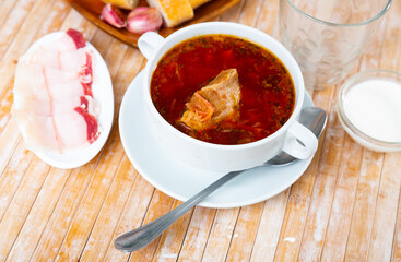 Borscht in bowl served on table with salo, garlic and smetana.