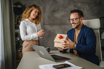 Female colleague give present to her male colleague in the office