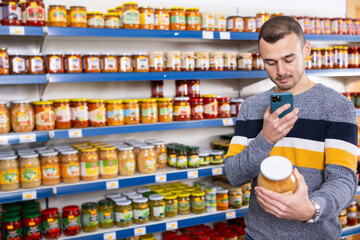 Adult male shopper with mobile phone choosing sauerkraut in grocery store
