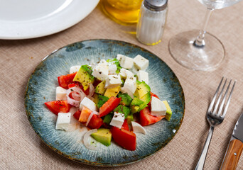 Service plate containing delicious salad with fresh avocado, tomato, cheese and sliced onion