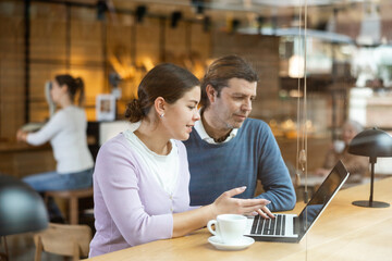 Focused man and woman drinking coffee while working on laptop in cozy cafe