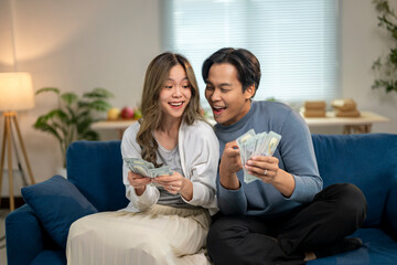 A man and woman are sitting on a couch, both holding money