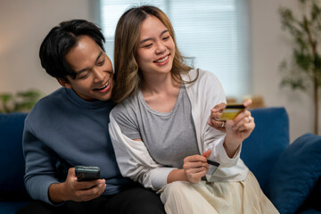 A man and woman are sitting on a couch, both holding up their cell phones