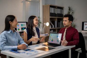Three people are sitting at a table with laptops and papers