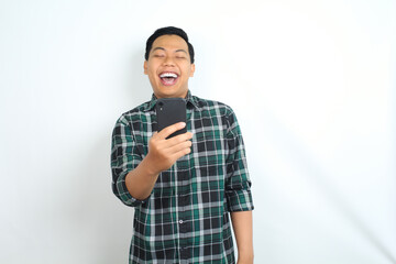 carefree asian man wearing casual plaid shirt laughing while watching video on smartphone isolated on white background