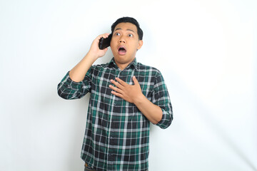 shocked asian man touching chest while talking on smartphone wearing casual shirt isolated on white background