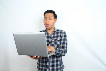 thoughtful asian man holding laptop looks confused and curious isolated on white background, male wearing plaid shirt using computer