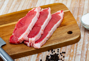 Raw piece of beef tenderloin with spices on wooden cutting board on light background