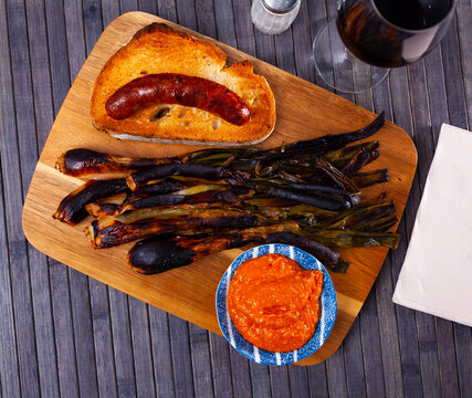 Traditional dishes of Catalonia, calcot with romesco sauce and grilled botifarra sausage served on wooden board.