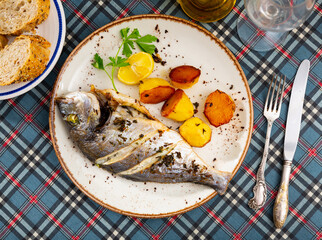 Whole Dorado fish and potatoes baked in oven served in a plate with parsley and lemon