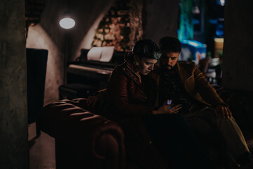 A couple sits closely on a cozy couch in a dimly lit room, sharing a contemplative moment. The intimate setting conveys warmth and relaxation.