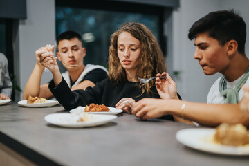 A group of high school students sitting around a table enjoying a meal together. The image captures a sense of camaraderie and togetherness among young friends during a shared dining experience.
