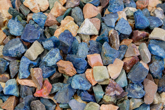 Background showing pile of colorful gemstones with natural pattern, creating beautiful texture. Colorful stones background. Collection of various raw gemstones in different colors and shapes, close up