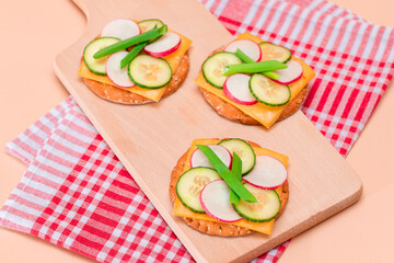 Light Breakfast. Quick and Healthy Sandwich. Fresh Cucumber and Radish with Green Onions and Cheese on Crispy Cracker on Wooden Cutting Board