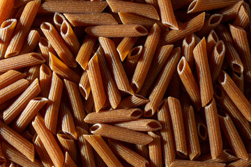 Uncooked Whole Grain Penne Rigate Pasta: A Culinary Canvas of Whole Wheat Macaroni, Creating a Lively and Textured Background for Gourmet Cooking. Whole Grain Dry Pasta. Whole Wheat Raw Macaroni