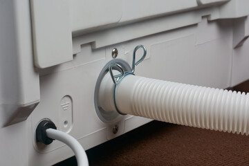 close-up of white flexible drain hose attached to washing machine back panel outlet with metal clamp, selective focus with copy space