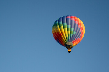 rainbow colored hot air balloon against blue sky with trees