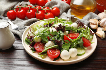 Tasty salad with arugula, lettuce, mozzarella cheese and vegetables on wooden table, closeup