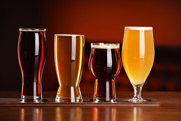 Glasses with different types of beer on wooden table against color background