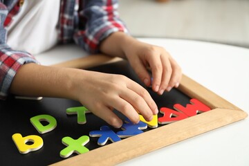 Little boy learning alphabet with magnetic letters at white table indoors, closeup