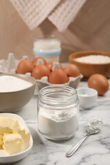 Baking powder in jar and other products on white marble table, closeup