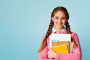 Study on college or school concept. Smiling teenage girl holds notebooks and charts and looks at empty space, isolated on blue background, studio shot