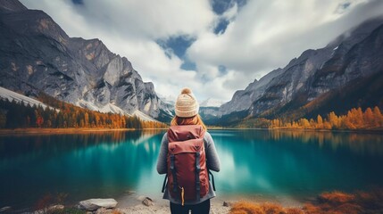 A person stands by a serene lake surrounded by mountains and autumn foliage.
